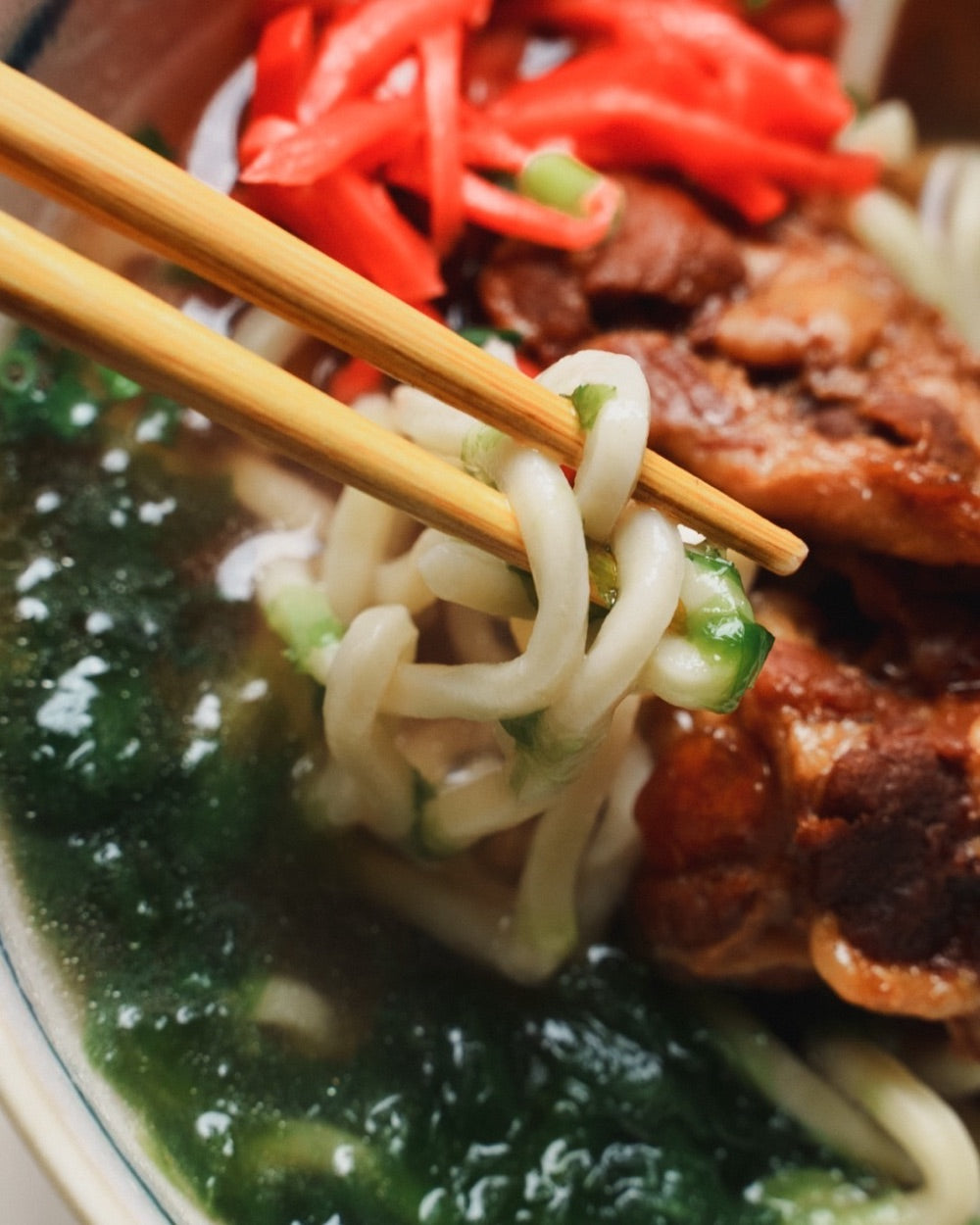 箸で持ち上げた自家製麺とソーキの沖縄そば